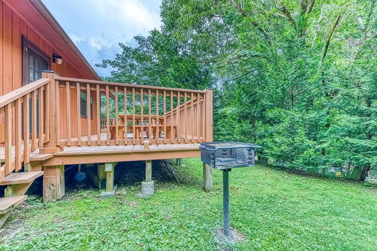 A broad view of the wooden back deck, featuring a charcoal grill and surrounded by dense, vibrant greenery. The scene is set for outdoor barbecues, al fresco dining, or simply relaxing in a serene, private natural setting.