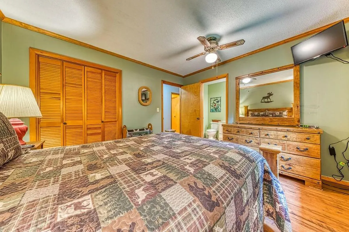 A bedroom featuring a comfortable bed, dresser, lamp, and closet doors. A mirror and a TV (not visible, but implied by the description) suggest it offers both relaxation and convenience, with soft lighting adding to the restful ambiance.