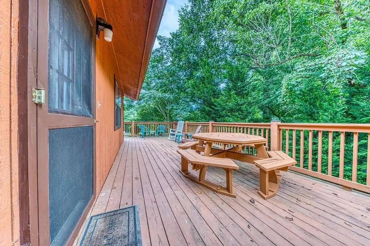 This image features a wooden picnic table on an outdoor deck, bordered by greenery and a screened door, suggesting a spot for group gatherings, outdoor dining, or evening activities like marshmallow roasting after exploring the nearby attractions.