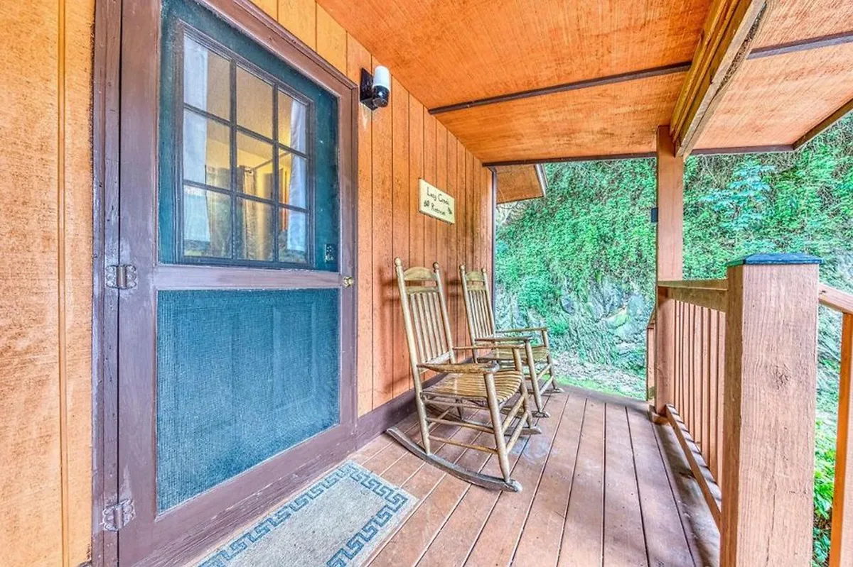 The image captures the cabin’s front porch with rocking chairs and a welcoming sign, framed by wooden walls and greenery. This inviting entryway encourages relaxation, socialization, and enjoyment of the peaceful setting after an adventurous day.