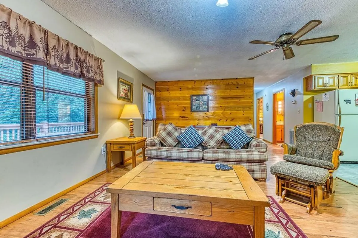 This image features a cozy living area with a plaid sofa, a wooden coffee table, and warm lighting from a lamp. The wooden walls and decorative artwork infuse the space with rustic charm, while the arrangement invites guests to relax, socialize, or play games together.