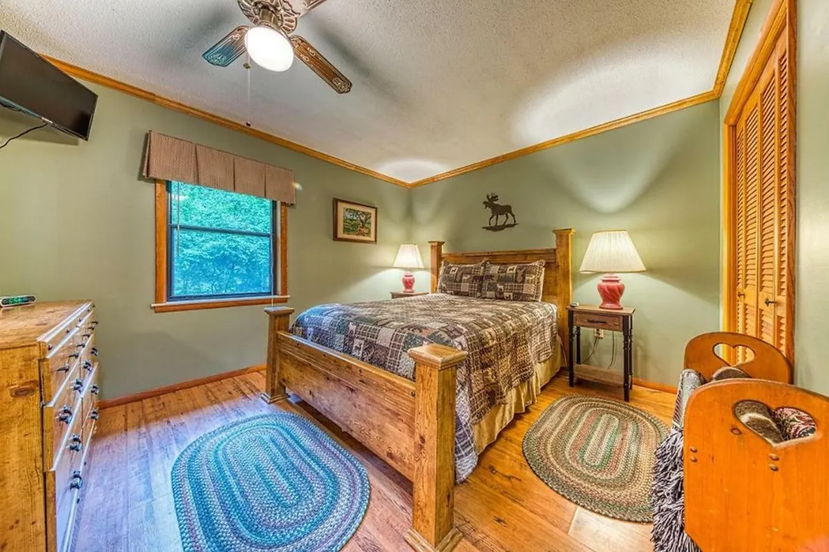 This image features a cozy wooden bed flanked by decorative lamps, a dressing table, and a window revealing the lush outdoor view. The calming atmosphere invites relaxation, with natural light streaming in and a sense of tranquil seclusion.