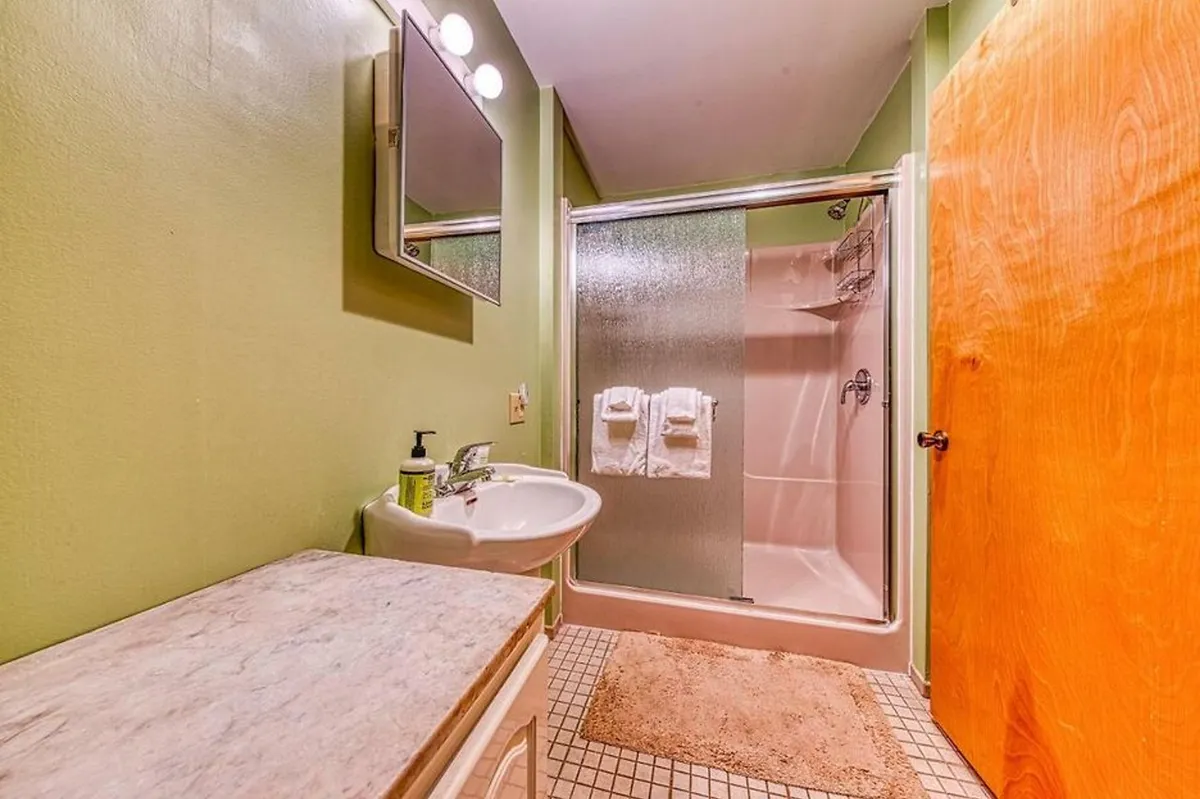 A full bathroom with a sink, shower stall, mirror, and wooden door. The space is bright and clean, ideal for refreshing after a day’s adventure or preparing for a restful night.