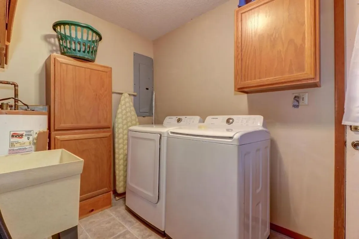 A functional and neatly organized laundry room featuring a washing machine, dryer, wooden cabinets, laundry basket, and ironing board. The setup ensures guests enjoy the practical benefits of a fully equipped cabin, making longer stays comfortable and carefree.
