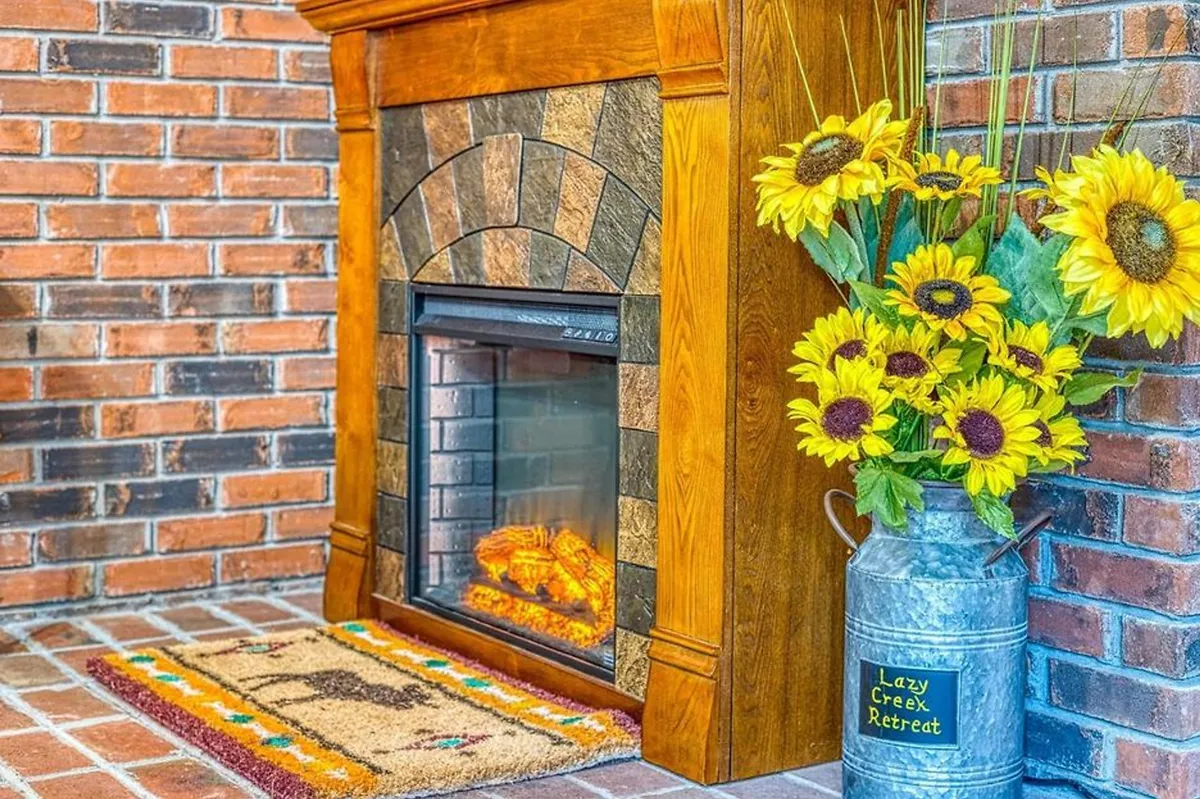 This interior shot showcases a rustic fireplace with a sunflower arrangement and a welcome mat, creating a focal point for socializing and storytelling. The setting feels intimate and perfectly suited for cozy evenings spent together.