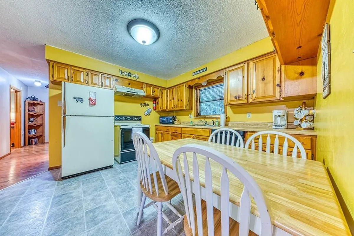 The image features a wooden dining table set against cheerful yellow walls, surrounded by wooden cabinets and modern kitchen appliances. The arrangement invites guests to imagine family meals, casual gatherings, or lively holiday celebrations in a cozy setting.